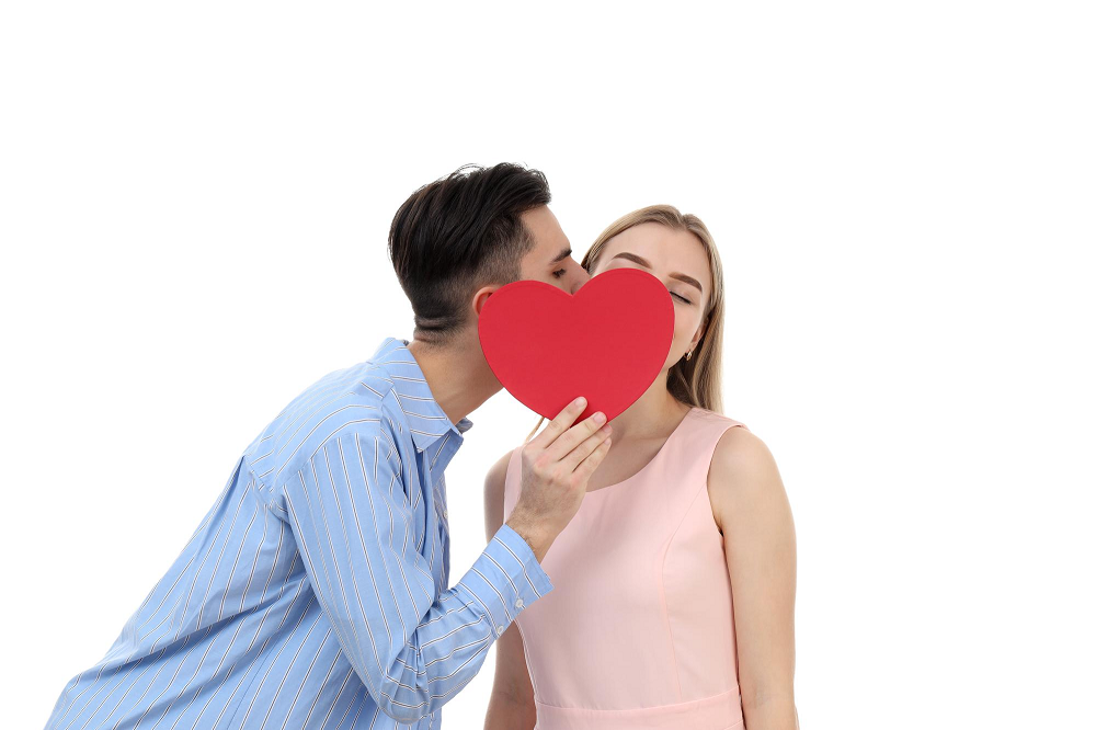 cómo hacer un amarre de amor casero: pareja de enamorados se besa y se tapa con un corazón